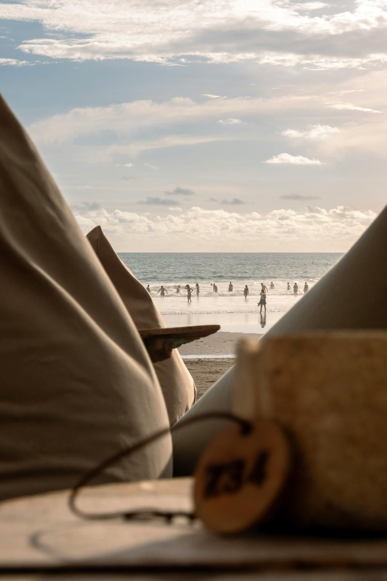 View of people at the beach with ocean in the background, framed by blurred bean bags and a drink in foreground.