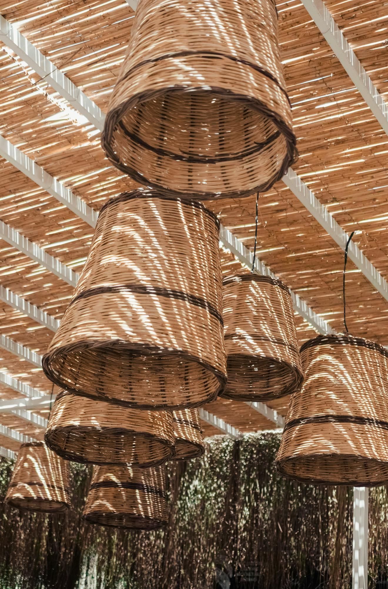 Woven basket lampshades hang from a slatted wooden ceiling, casting patterned shadows below.